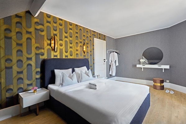 A modern hotel room with a large bed, a bedside table with a vase, a wall-mounted towel rack, and a round mirror on a shelf. - RESIDENCE WAVES Paris Orly Aéroport (Villeneuve-Saint-Georges)