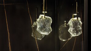 Un baño con un lavamanos grande de mármol oscuro y dos lámparas geométricas transparentes colgantes.