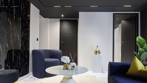 Una sala de estar moderna con una pared de mármol, una mesa redonda de centro, un sofá azul y una puerta oscura.
