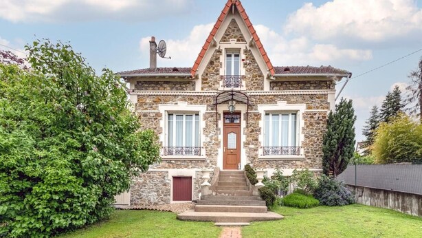 Una casa de piedra con techo inclinado y una entrada central con puerta, además de un pequeño balcón.