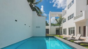 A modern pool area with a clear blue pool, white walls, and a few lounge chairs.