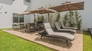 A patio with outdoor furniture, including chairs and a lounge chair, under umbrellas.