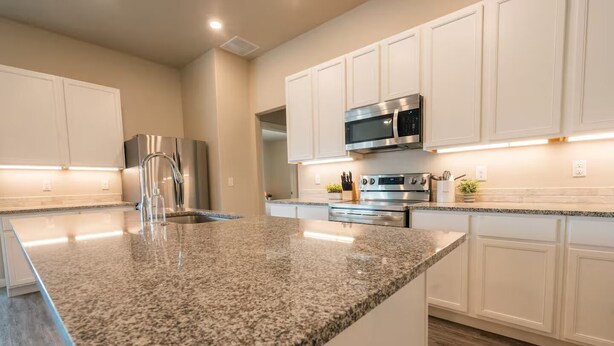 A modern kitchen with granite countertops, stainless steel appliances, and white cabinetry. - The Slowdown Saddle - Hot Tub (Lubbock)