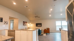 A spacious kitchen with a central island, a dining area with a table and chairs, and a living area with a sofa. - The Slowdown Saddle - Hot Tub (Lubbock)