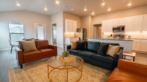 A modern living room with a brown leather sofa, a dark green sofa with cushions, and a round glass coffee table. - The Slowdown Saddle - Hot Tub (Lubbock)