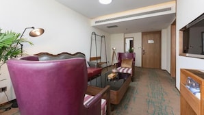 Una habitación de hotel con un sillón morado, un sofá, una mesita y un televisor.