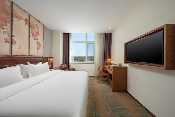 A hotel room with a large bed, a desk, a television, and a world map on the wall.