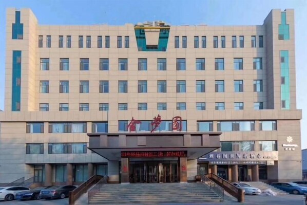 Un edificio de varios pisos con una entrada destacada, un letrero grande sobre la entrada y varias ventanas.