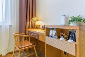 A small, neatly arranged workspace with a wooden desk, a chair, a lamp, a coffee maker, and a shelf with cups and a plant. - Jin Meng Yuan Hotel (Zibo)