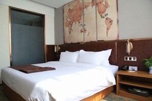 Una habitación de hotel con una cama grande, un mapa mundial en la pared, un cabecero de madera y una mesita de noche con un teléfono y una planta.