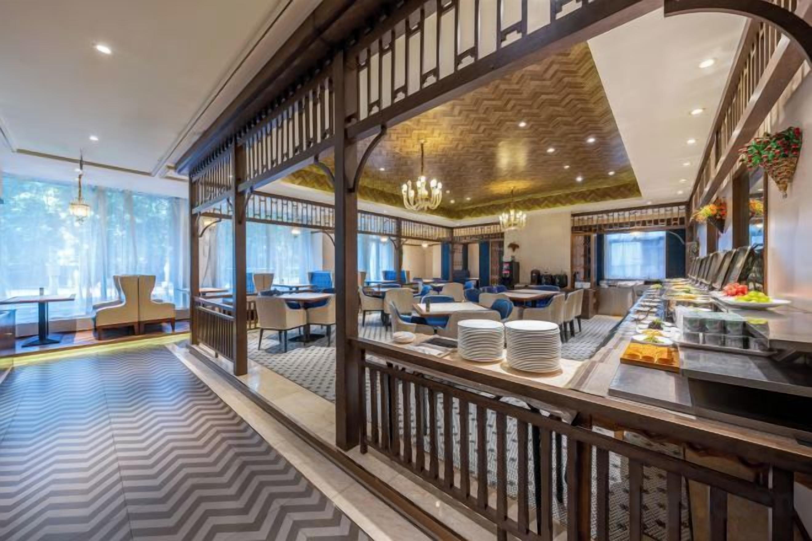 A modern restaurant with a long counter, multiple seating areas, and a decorative railing.