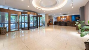 Un vestíbulo espacioso con un diseño moderno de techo circular, grandes puertas de cristal que dan al exterior y una zona de recepción con mostrador de madera.