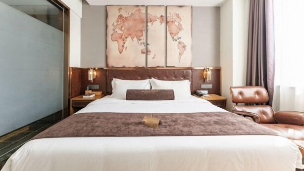 Una habitación de hotel con una cama grande, un mapa mundial en la pared y un sillón de cuero.