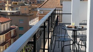 Un balcon avec une table et des chaises, donnant sur un paysage urbain composé d’immeubles aux toits de tuiles.