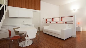 A modern kitchen with white cabinets, a dining area with a round table and chairs, and a white sofa in a living area. - Desuite Bolsena Loft (Milan)