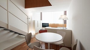 A modern hotel room with a white dining table, four chairs, a sofa, a TV, and a lamp. - Desuite Bolsena Loft (Milan)