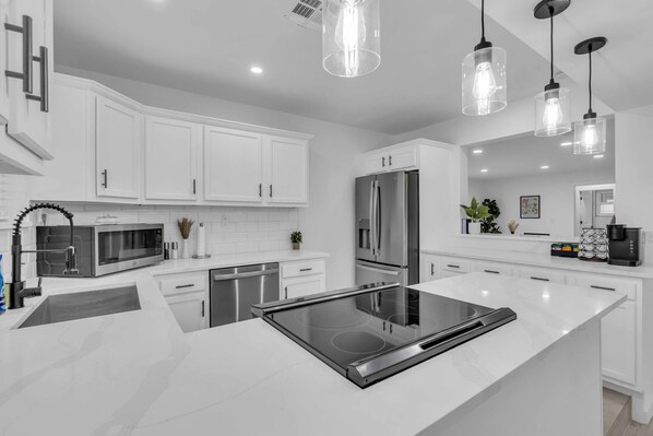 A modern kitchen with white cabinetry, stainless steel appliances, and pendant lighting.