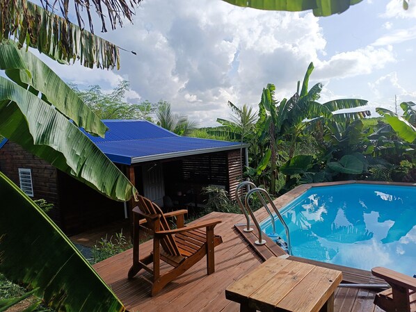 A wooden deck with a pool, surrounded by lush greenery and a blue-roofed structure. - belle créole (Anse-Bertrand)