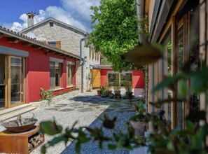 A courtyard with stone flooring, potted plants, and a red building with wooden shutters. - Poolside Grand Retreat Villa (Sveti Lovrec)
