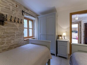 A bedroom with a stone wall, two beds, a wardrobe, and a small bedside table with a lamp. - Poolside Grand Retreat Villa (Sveti Lovrec)