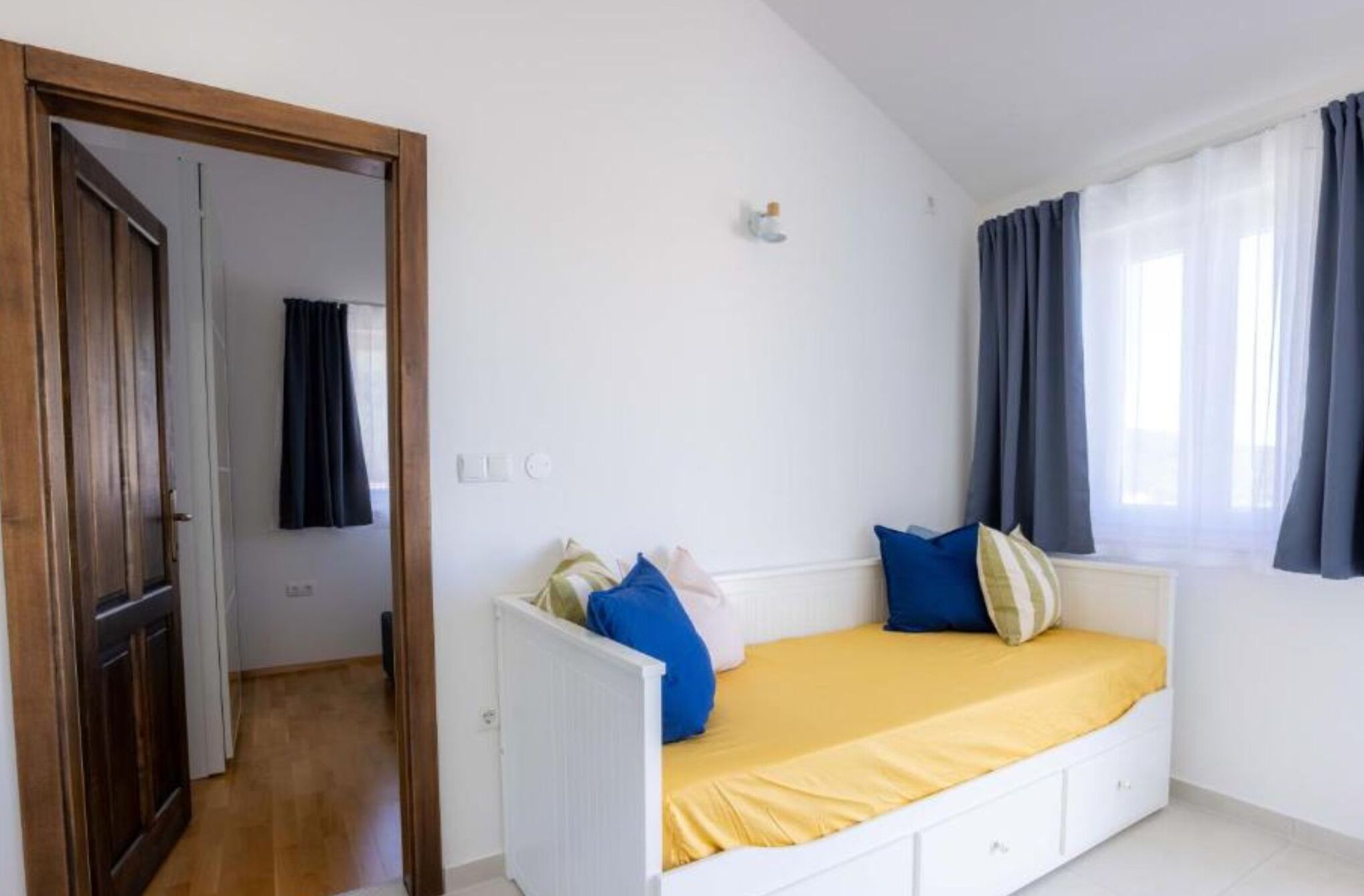 Un dormitorio con una cama blanca, una puerta de madera y un ventanal con cortinas.