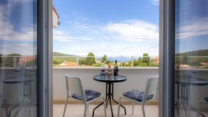 Ein Balkon mit zwei Stühlen und einem Tisch, der auf eine reizvolle Landschaft mit Hügeln und einem Gewässer blickt.