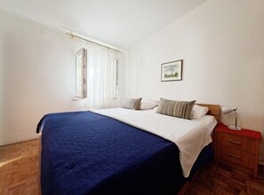 Une chambre à coucher avec un lit, une table de chevet, une lampe, une fenêtre avec des rideaux et un tableau au mur.