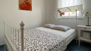 A bedroom with a bed, a nightstand, a lamp, a window with curtains, and a painting on the wall. - Apartments Lara Rab - One Bedroom Apartment with Balcony (Rab)