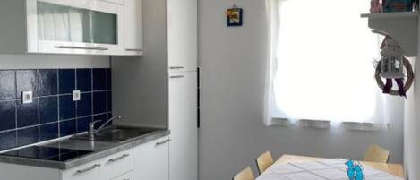 A compact kitchen with white cabinets, a black countertop, and a window with sheer curtains.