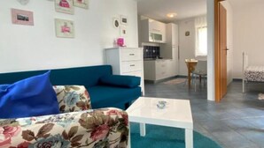 A compact living space with a sofa, a small table, a kitchenette, and a bed. - Apartments Lara Rab - One Bedroom Apartment with Balcony (Rab)