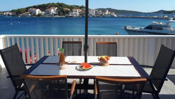 Une table entourée de chaises et protégée par un parasol, avec vue sur une marina où sont amarrés des bateaux et sur une ville située au loin.