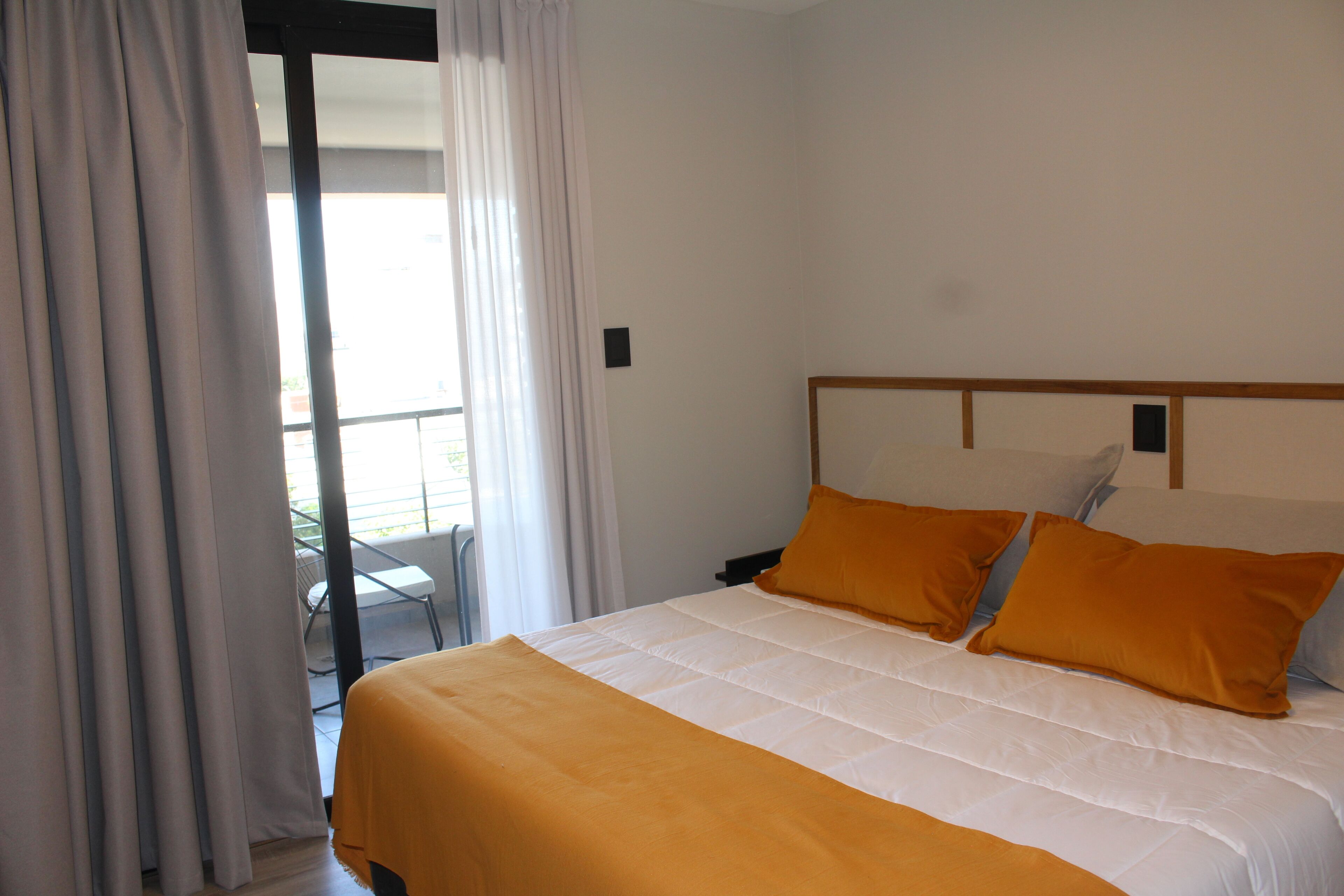 A hotel room with a bed, white curtains, and a view of the outdoors.
