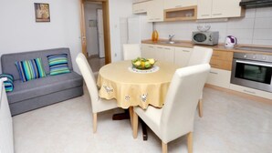 A compact living space with a dining area featuring a round table with a yellow tablecloth and a bowl of fruit. There is a gray sofa with striped cushions and a small framed picture on the wall. - One-Bedroom Apartment With Terrace And Sea View (A1) (Trogir)