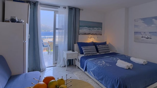 Une chambre à coucher avec un lit, une table de chevet, une chaise, une table avec des fruits et une vue sur la mer.