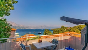 Un balcon avec une table et des chaises, offrant une vue sur la côte, avec des bateaux et des montagnes en toile de fond.