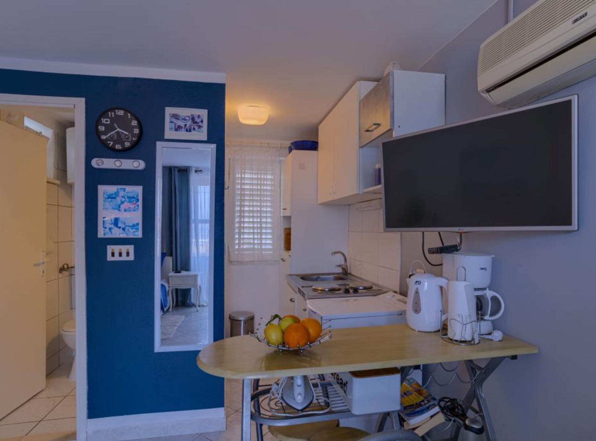 Una cucina compatta con un tavolo da pranzo, una sveglia e una televisione a schermo piatto.