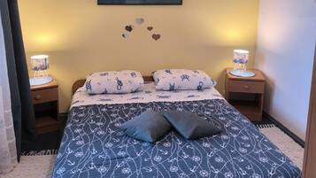 A bedroom with a bed, two bedside tables, a hanging lamp, a wall painting, and heart-shaped decorations.