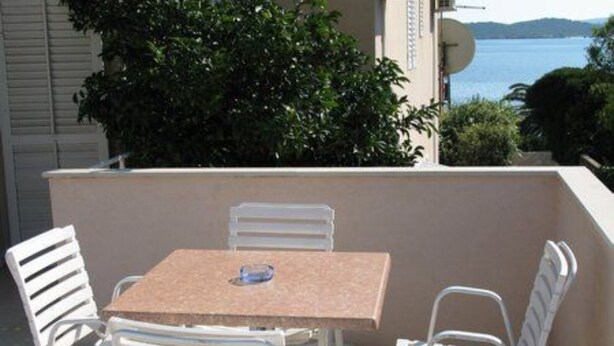 A balcony with a table and chairs, overlooking a body of water and greenery. - Seafront Apartments Pretner - Studio with Terrace (Orebic)