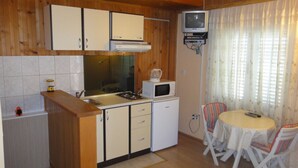 A compact kitchen with wooden cabinets, a microwave, a small refrigerator, a gas stove, and a dining area with a table and chairs. - Seafront Apartments Pretner - Studio with Terrace (Orebic)