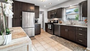 A modern kitchen with dark cabinets, stainless steel appliances, and a large window providing natural light. - Lake Cottage Retreat-Hot Tub-Game Room (Avon Lake)
