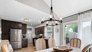 A modern kitchen with dark cabinets, stainless steel appliances, and a dining area with a white table and chairs. - Lake Cottage Retreat-Hot Tub-Game Room (Avon Lake)