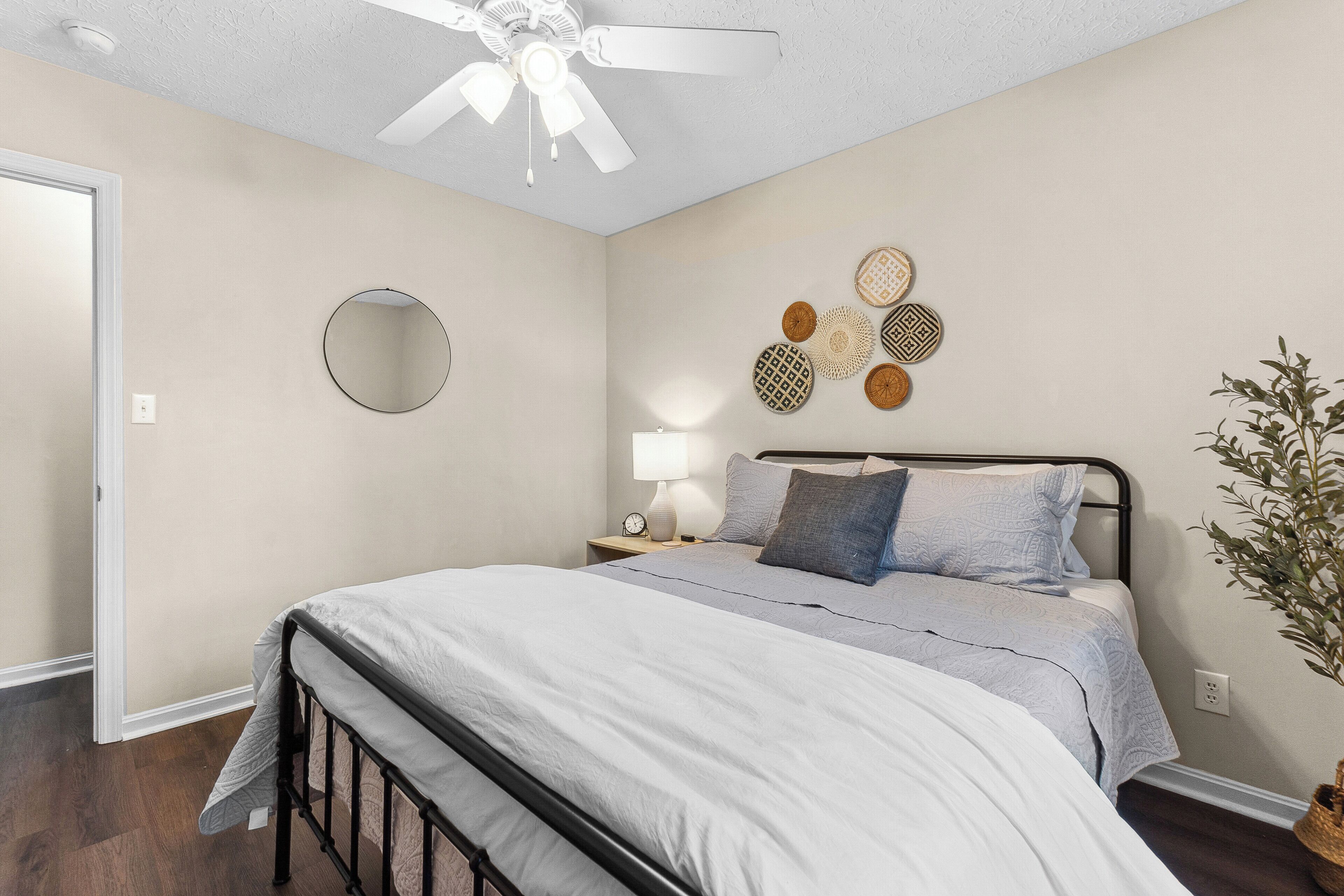 A bedroom with a bed, a ceiling fan, a bedside table with a lamp, and decorative wall art.