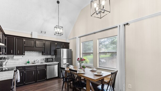 A modern kitchen with dark cabinets, stainless steel appliances, and a wooden dining table with chairs. - Beautiful home in delightful Perry w/ King Bed (Perry)
