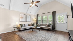 A spacious living room with a high ceiling, a ceiling fan, a large window with curtains, a sofa set, a coffee table, and a rug. - Beautiful home in delightful Perry w/ King Bed (Perry)