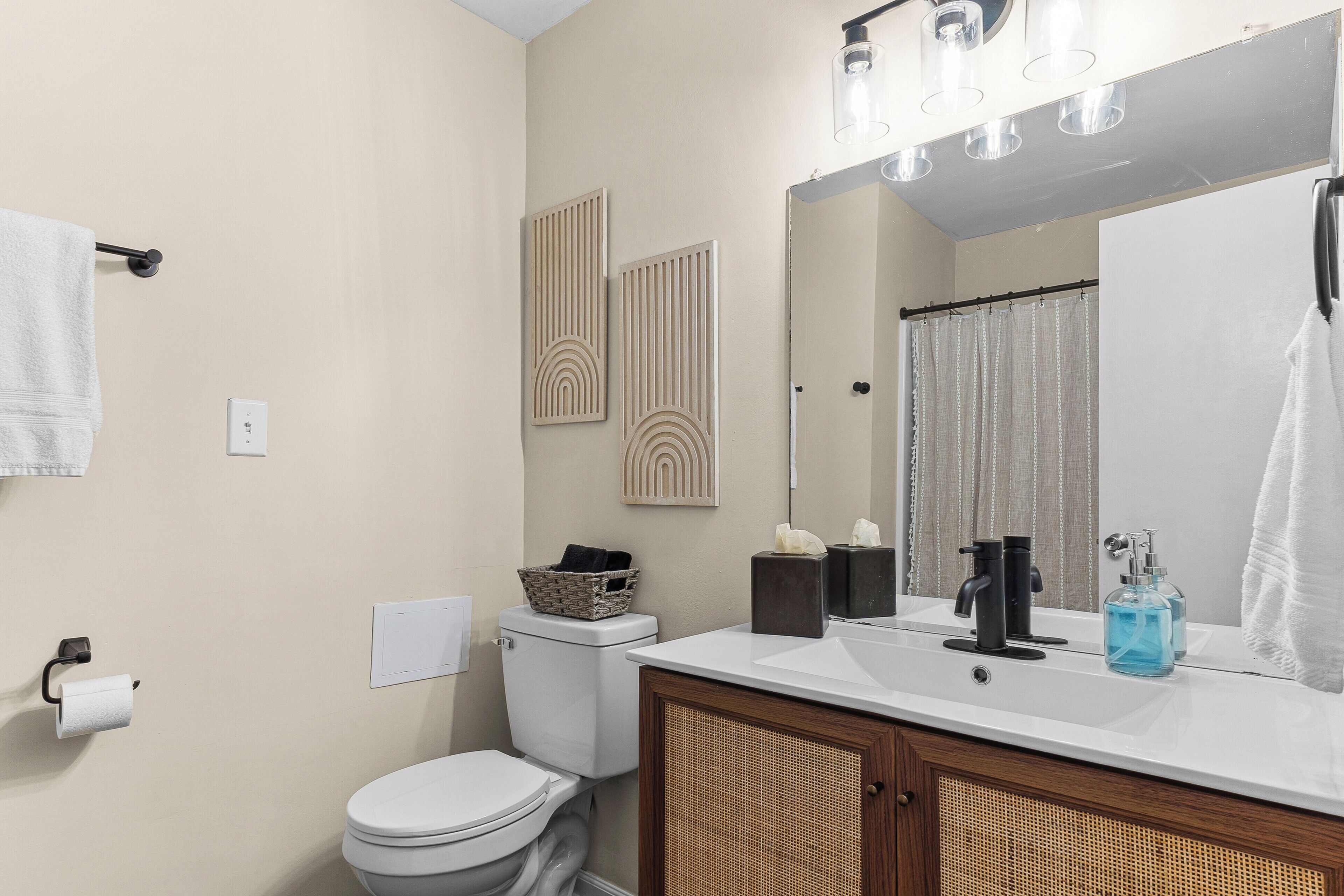 A bathroom with a toilet, sink, mirror, towel rack, and decorative wall panels.
