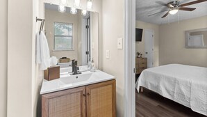 A bathroom with a white sink, wooden cabinets, a mirror, and a ceiling fan. - Beautiful home in delightful Perry w/ King Bed (Perry)