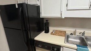 Una cucina compatta con mobili bianchi, un frigorifero nero, una lavastoviglie e un lavello.