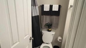 Un bagno piccolo e stretto con il water bianco, un cestino nero e un tappeto nero sul pavimento.