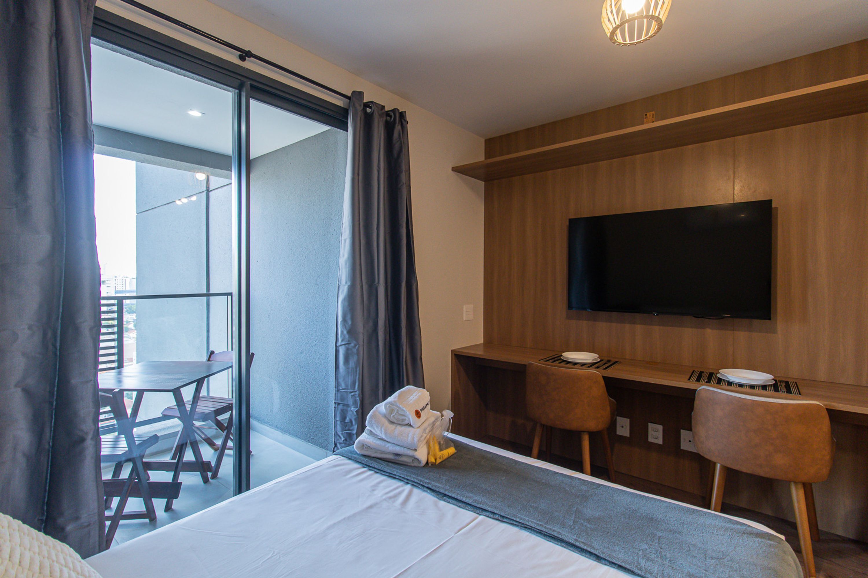 Une chambre d’hôtel comprenant un lit, un bureau avec deux chaises, un téléviseur à écran plat et un balcon avec une table et des chaises.