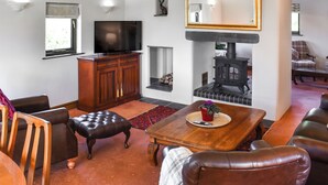 A living room with a fireplace, a television, and leather furniture. - Church View Apartment (Parkham, near Bideford)